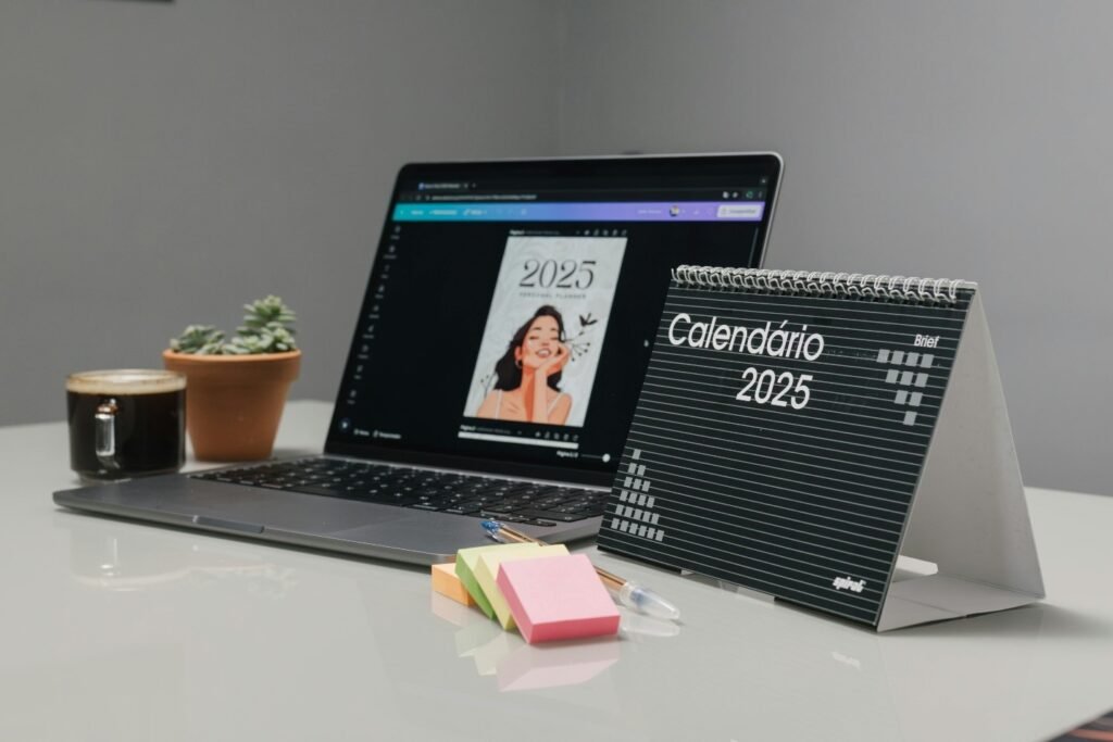 Desk setup featuring a 2025 calendar, a laptop displaying a planner cover, a small potted succulent, a cup of coffee, sticky notes, and a pen on a clean, modern workspace.